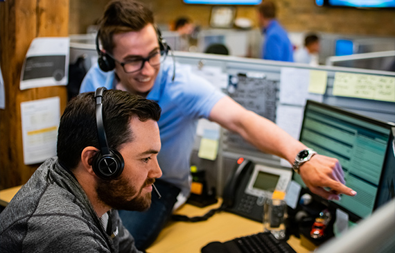 Two employees at Beacon Funding look at a computer screen and discuss how they help a customer get approved for financing.