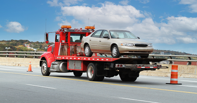 A tow truck driver keeps the road safe by hauling a four-door vehicle in their red tow truck.