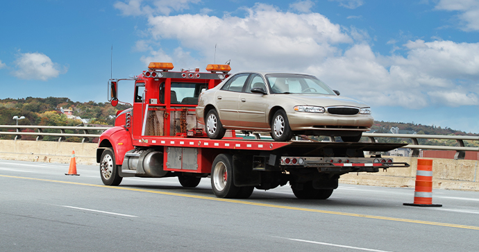 A tow truck driver keeps the road safe by hauling a four-door vehicle in their red tow truck. A tow truck driver keeps the road safe by hauling a four-door vehicle in their red tow truck.