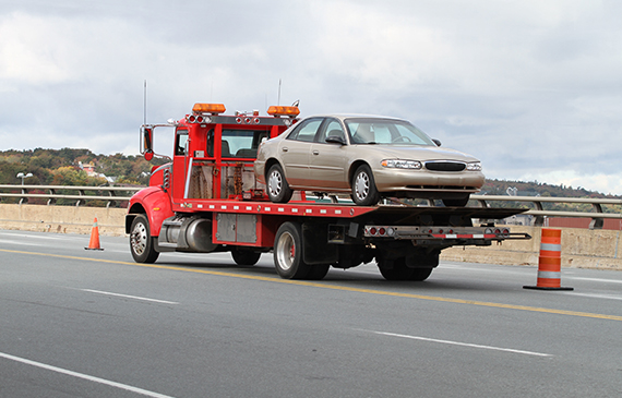 A red tow truck hauls a small 4-door vehicle after receving an emergency phone call. A red tow truck hauls a small 4-door vehicle after receving an emergency phone call.