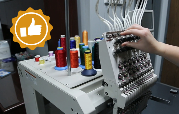 An operator tunes a sewing machine with multiple colored threads in the background.