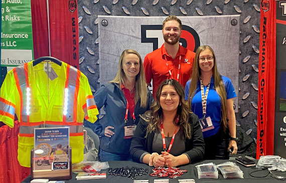 Members of Beacon Funding and Transit Pro stand in front of a tradeshow booth at the American Towman Expo 2023.