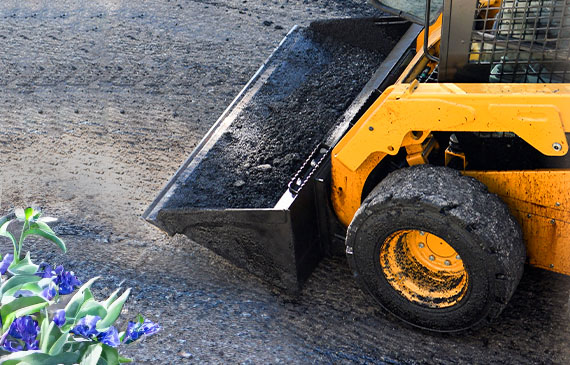 A yellow skid steer hauls a bucket of dirt over a ground plot. A yellow skid steer hauls a bucket of dirt over a ground plot.