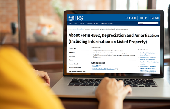 Over the shoulder view of a business owner using their laptop to visit the IRS's website to download Form 4562. Their screen says in bold black letters, Depreciation and Amortization. Over the shoulder view of a business owner using their laptop to visit the IRS's website to download Form 4562. Their screen says in bold black letters, Depreciation and Amortization.