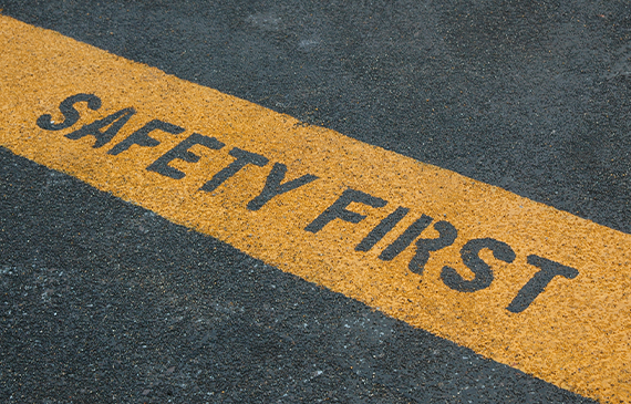 Closeup of a paved road with a yellow line that reads "Safety First" in large, uppercase letters. Closeup of a paved road with a yellow line that reads "Safety First" in large, uppercase letters.