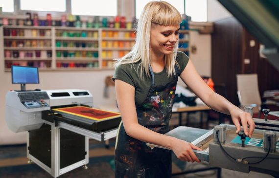 A business owner smiles as she prepares a fresh print using a screen exposure direct-to-screen computer system. A business owner smiles as she prepares a fresh print using a screen exposure direct-to-screen computer system.