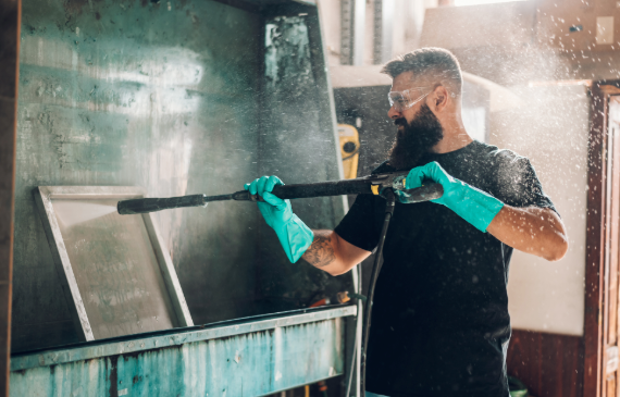A small business owner uses a high-pressure washer in a washout booth to clean a screen. A small business owner uses a high-pressure washer in a washout booth to clean a screen.