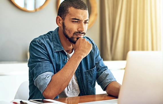 A concerned-looking young business owner looks at their laptop on their wooden desk as he considers whether to apply for equipment financing. A concerned-looking young business owner looks at their laptop on their wooden desk as he considers whether to apply for equipment financing.