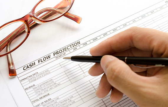Hand holding a pen while reviewing a cash‑flow projection worksheet next to eyeglasses. Illustrates how Beacon Funding’s equipment financing supports better cash‑flow planning by spreading equipment costs over time, enabling businesses to grow without straining their budget.
