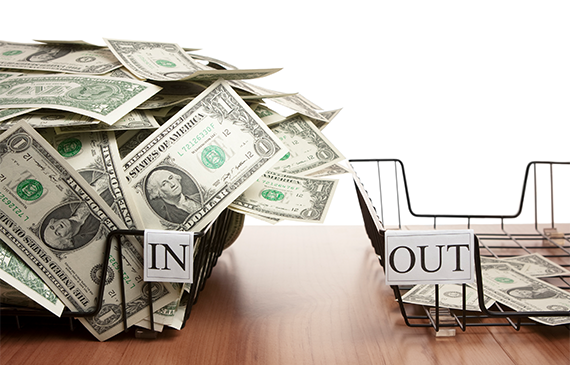 Two office trays labeled ‘In’ and ‘Out,’ with the ‘In’ tray overflowing with cash and the ‘Out’ tray nearly empty, symbolizing strong cash flow. Represents how financing equipment with Beacon Funding helps businesses preserve working capital, maintain steady cash flow, and avoid large upfront costs.