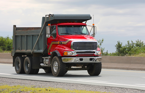 Red dump truck driving down the highway, representing how Beacon Funding’s equipment financing makes it easier for businesses to upgrade or add trucks to their fleet to boost productivity.