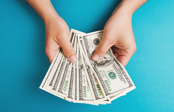Hands holding U.S. dollar bills against a blue background, illustrating the choice between paying cash or using Beacon Funding equipment financing to preserve working capital. Hands holding U.S. dollar bills against a blue background, illustrating the choice between paying cash or using Beacon Funding equipment financing to preserve working capital.
