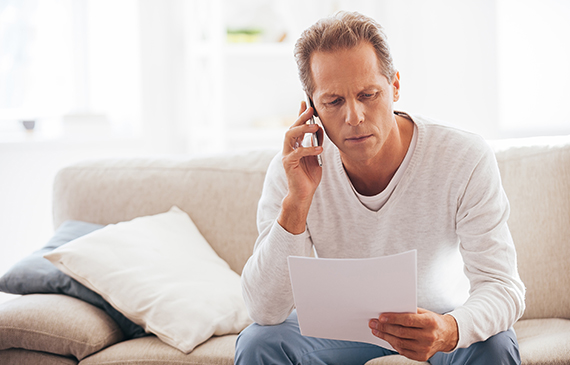 A businessman talks on the phone while holding equipment financing documents.