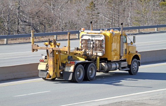 A used, yellow heavy-duty tow truck drives down the highway after getting financed by Beacon Funding.