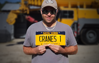 Dave Sandel Jr stands with a New York vehicle license plate that reads "CRANES 1"