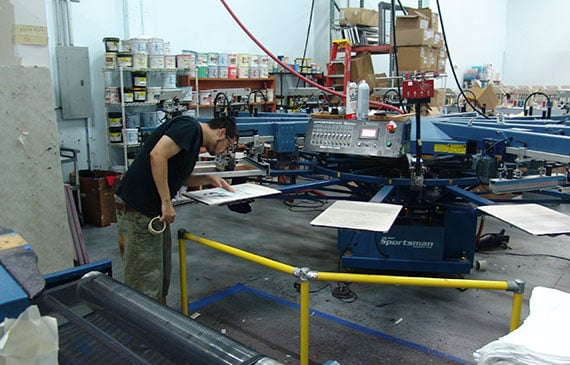 A worker inspects his print on a printing press machine.