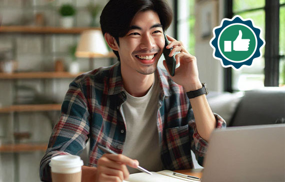 Person smiling while talking on a phone, sitting at a table with a laptop and coffee cup. Thumbs-up icon is visible. Person smiling while talking on a phone, sitting at a table with a laptop and coffee cup. Thumbs-up icon is visible.