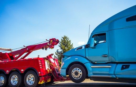 A heavy wrecker with a rotator recently financed by Beacon Funding tows a large blue semi truck after a wreck.