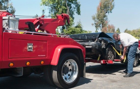 A red wheel-lift tow truck lifts an alternative fuel vehicle in the air and prepares it for towing. A red wheel-lift tow truck lifts an alternative fuel vehicle in the air and prepares it for towing.