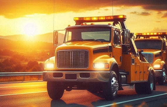 Two yellow tow trucks drive on a highway at sunset, with hills in the background. Two yellow tow trucks drive on a highway at sunset, with hills in the background.