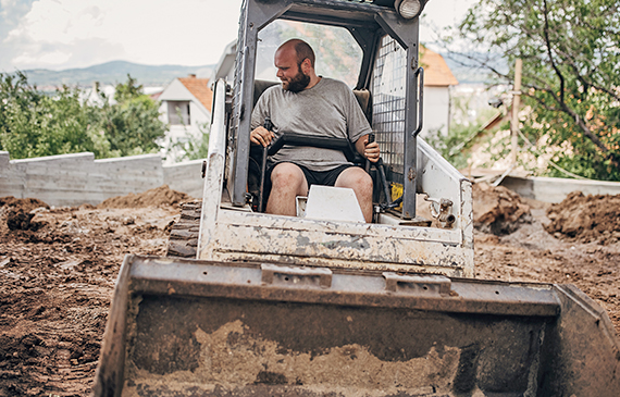 A skid steer operator uses a bucket attachment to excavate for their landscaping project.