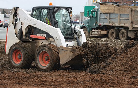 A skid steer operator uses a bucket attachment to dig up gravel for their landscaping project.