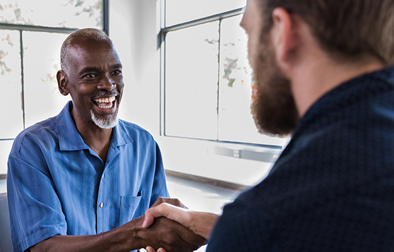 Two smiling business owners shake hands after financing equipment together.