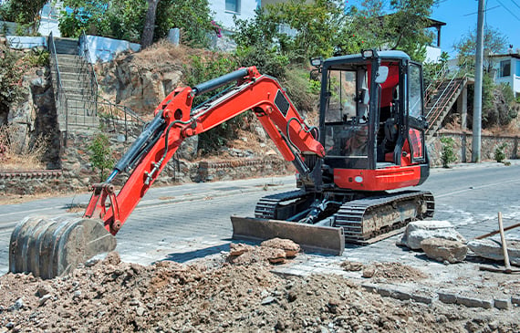 A red mini excavator sits on a road during a digging project.