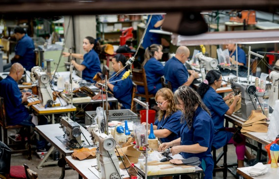 A production floor of workers dressed in blue uniforms diligently work using decorated apparel equipment.