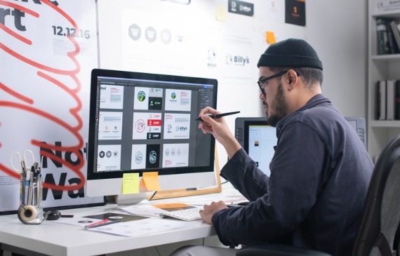 A graphic designer works on their desktop computer to design multiple t-shirts at once using new computer software.